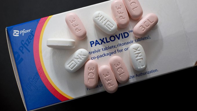 A photo of several pink and white oval pills sitting on top of a Paxlovid box.