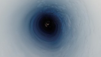 A photo looking into a drill hole in West Antarctica. White ice is seen on the edges of the frame which turns into a gradient of light blue to dark blue in the center circle of the image.