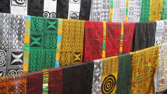 A photo of a variety of different colored textiles with adinkras, used in Ghana's Twi language to express proverbs, stamped in black ink.