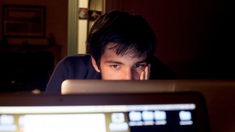 A teen looks sadly at a laptop screen in a dark room.