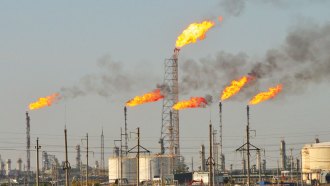 Five natural gas flares burn along the horizon of an oil refinery.